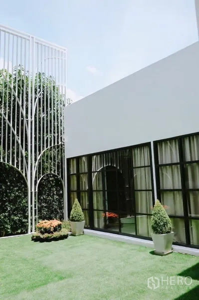 บ้าน ให้เช่าในHuai Khwang, Bangkok - บ้านเดี่ยวสีขาวสไตล์โมเดิร์น หน้าต่างกรอบดำ เปิดสู่สนามหญ้าและซุ้มเหล็กตกแต่ง