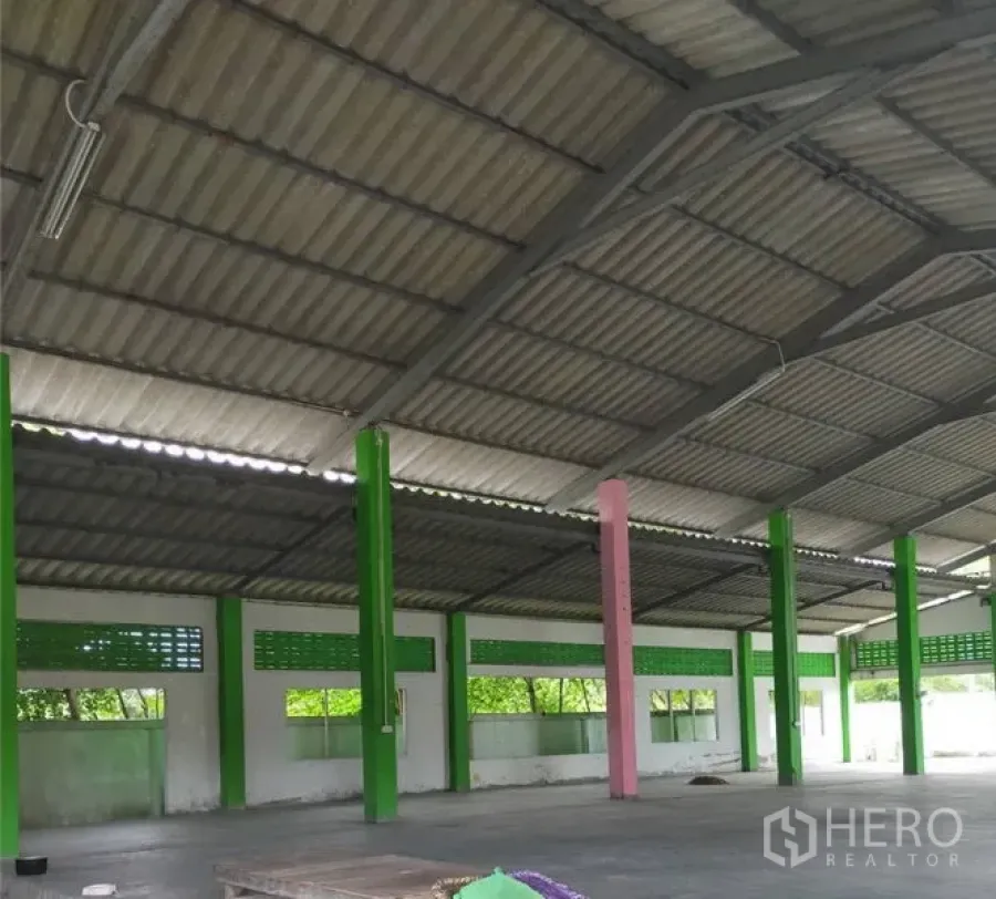 Factory for rent or sale in Samut Prakan - Spacious factory hall with high metal roof, green support columns, ventilation blocks and concrete floor.