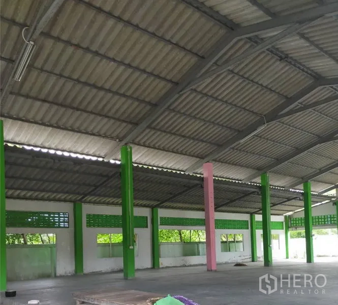 Factory for rent or sale in Samut Prakan - Spacious factory hall with high metal roof, green support columns, ventilation blocks and concrete floor.