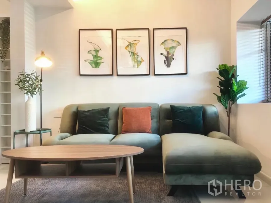 Townhouse for rent or sale in Bang Phli, Samut Prakan - Bright living room with green sectional sofa, wooden coffee table, and framed botanical artwork.