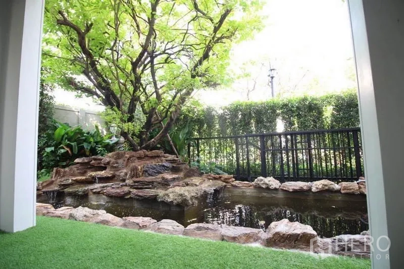 Detached House for rent or sale in Lat Phrao, Bangkok - Private garden with mature tree and rock-edged pond behind a black fence.