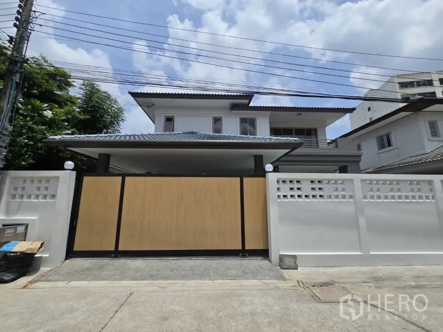 Detached House for sale in Suan Luang, Bangkok - Street view of the detached house with white perimeter wall and wide sliding wooden gate.