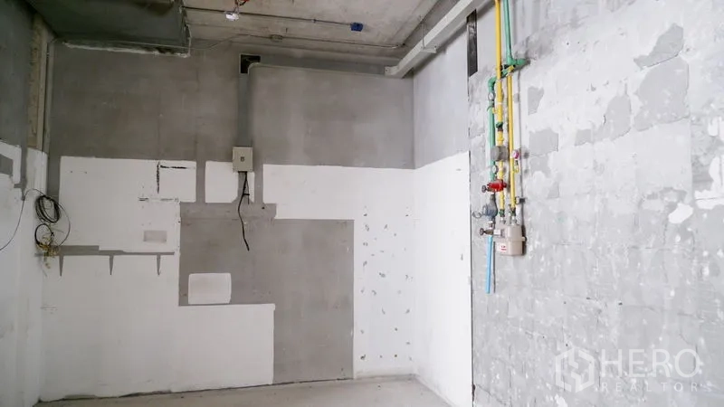 Retail Space for rent in Watthana, Bangkok - Service wall with utility conduits and wiring in a bare retail interior with cement finish.