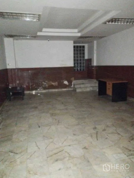 Shophouse for rent in Watthana, Bangkok - Spacious room with marble-look flooring, step-up area and basic office desks.