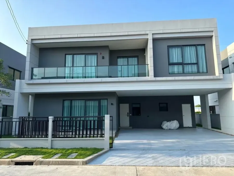 Detached House for rent in Bang Phli, Samut Prakan - Front elevation of the detached house with balcony railing, wide driveway and small lawn.