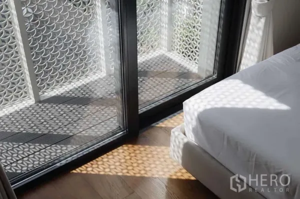 Townhouse for rent or sale in Watthana, Bangkok - Bedroom balcony with decorative lattice screen casting patterned sunlight on the wood floor.