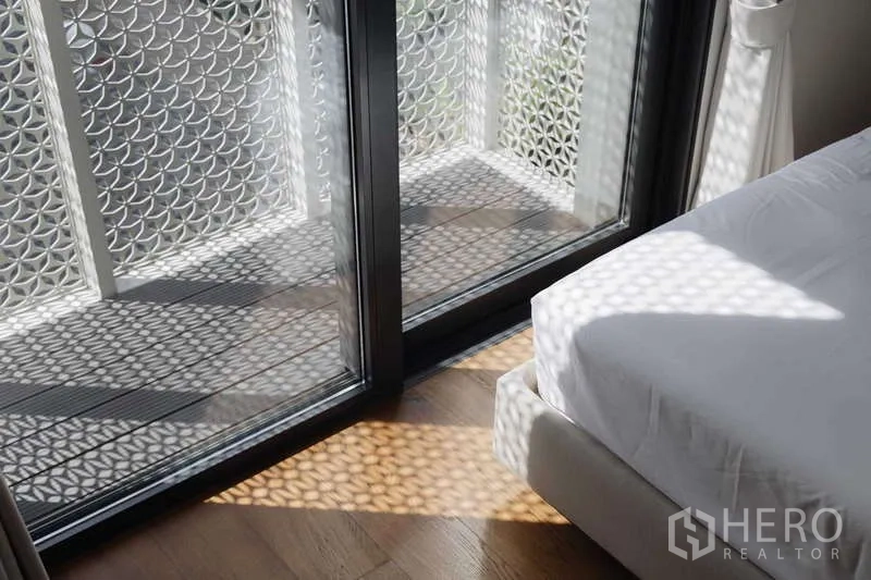 Townhouse for rent or sale in Watthana, Bangkok - Bedroom balcony with decorative lattice screen casting patterned sunlight on the wood floor.