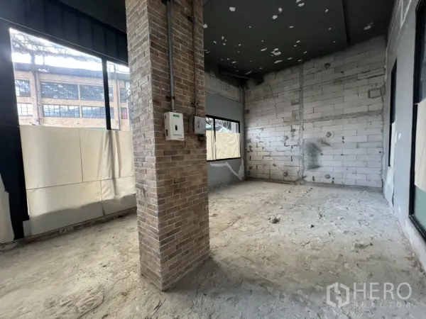 Retail Space for rent in Khlong Toei, Bangkok - Corner retail area with brick pillar, multiple windows and rough concrete flooring ready for fit-out.