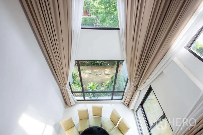 Detached House for rent or sale in Kanchanaburi - Double-height living area with floor-to-ceiling windows overlooking a green garden.