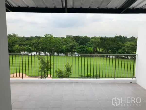 Townhouse for sale in Bang Kapi, Bangkok - Spacious tiled balcony with black railing overlooking lush green fairways, trees, and a reflective pond.