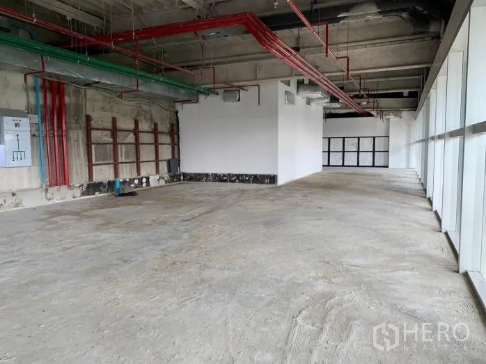 Retail Space for rent - Long rectangular retail shell with red and green service pipes, electrical panels and a glazed facade.