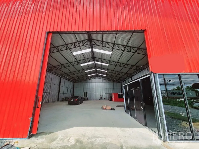 Warehouse for rent in Sam Phran, Nakhon Pathom - Large entrance with red sliding door and adjacent glass entry leading into the warehouse.