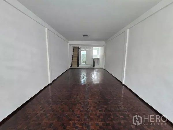 Shophouse for rent in Watthana, Bangkok - Open‑plan retail floor with dark wood flooring leading to a staircase and service area.