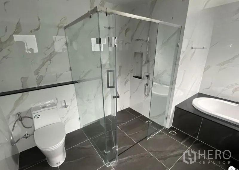 Detached House for rent in Bang Phli, Samut Prakan - Contemporary bathroom featuring a glass shower enclosure, bathtub, and marble-look tiles.