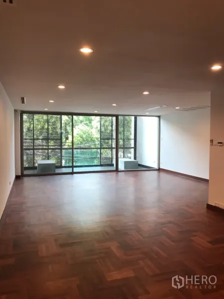 Home Office for rent in Watthana, Bangkok - Spacious open-plan living or workspace with parquet floors and full-height windows opening to a balcony.