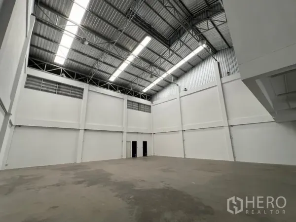 Warehouse for rent in Phra Samut Chedi, Samut Prakan - Spacious warehouse interior with high steel truss roof, skylights and white walls.