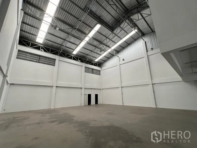 Warehouse for rent in Phra Samut Chedi, Samut Prakan - Spacious warehouse interior with high steel truss roof, skylights and white walls.
