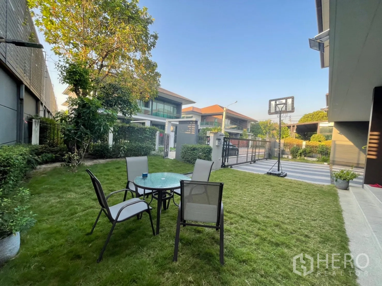 Detached House for rent or sale in Bang Kapi, Bangkok - Landscaped front yard with outdoor table set on grass and a portable basketball hoop near the gate.