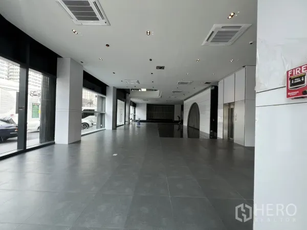Retail Space for rent in Watthana, Bangkok - Spacious open-plan retail hall with floor-to-ceiling windows, gray tiles, and ceiling-mounted air-conditioning.