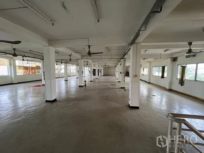 Shophouse for rent in Khlong Toei, Bangkok - Expansive open-plan upper floor with rows of columns, ceiling fans and windows providing natural light.