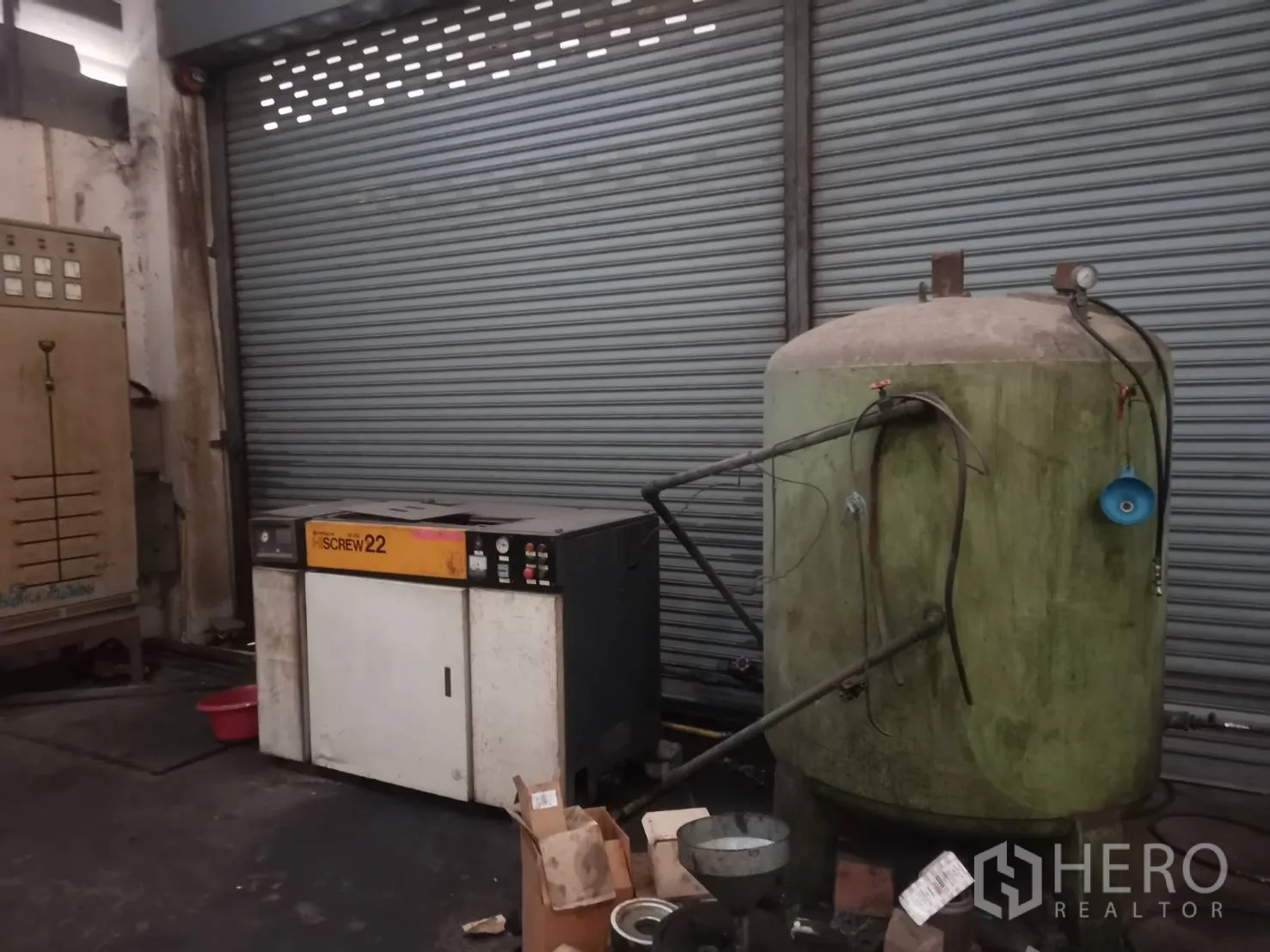 Factory for rent or sale in Bang Khun Thian, Bangkok - Air compressor and storage tank positioned near a roller shutter door.