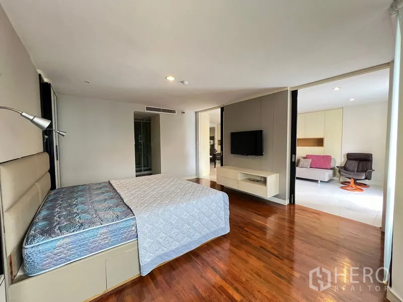 Condominium for rent or sale in Khlong Toei, Bangkok - Spacious bedroom with wood floors, bed and TV opening to the living area.