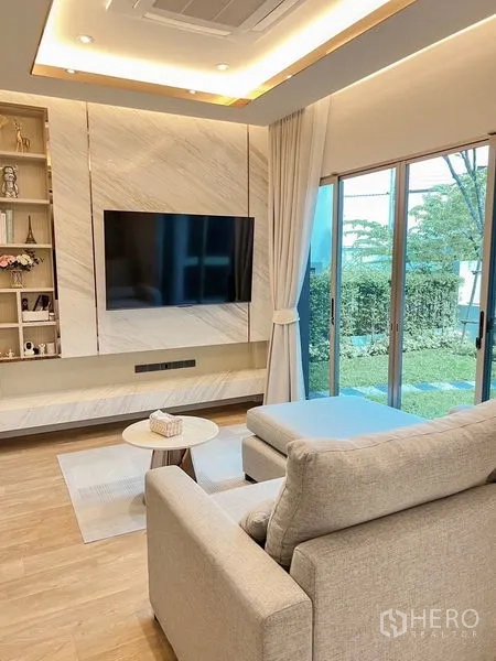 Detached House for sale in Bang Kapi, Bangkok - Cozy family room with built-in TV wall, chaise sofa and sliding doors opening to the lawn.