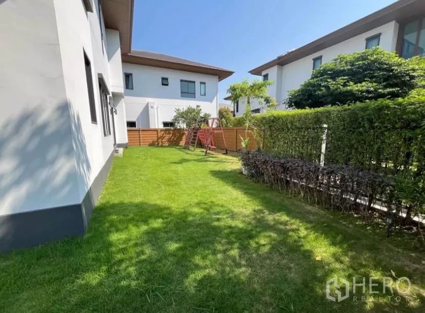 Detached House for rent in Prawet, Bangkok - Sunny backyard with green lawn, hedge fence and a wooden play set in a quiet estate.