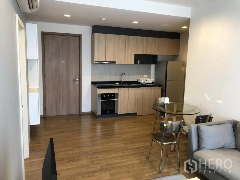 Condominium for rent in Watthana, Bangkok - Open-plan kitchen with wood cabinetry, built-in cooktop, oven and full-size refrigerator.