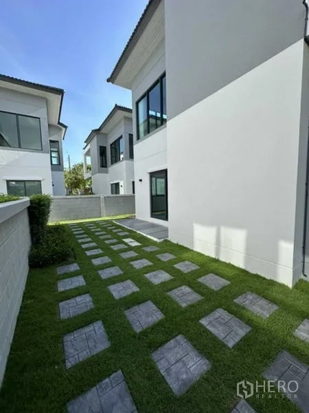 Detached House for rent in Bang Phli, Samut Prakan - Side lawn with stepping stones along the white exterior wall of the home.