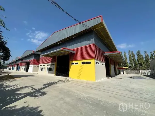 Warehouse for rent in Lam Luk Ka, Pathum Thani - Row of new warehouse units with multiple loading bays and a spacious access road inside a secure industrial compound.