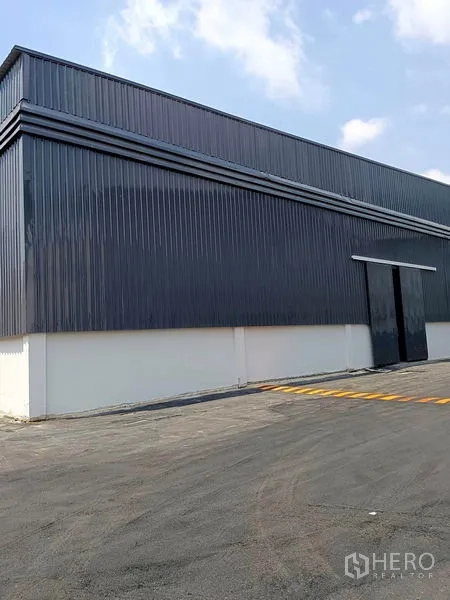 Warehouse for rent in Khlong Toei, Bangkok - Front facade of warehouse with large sliding metal door and a speed bump on the paved apron.