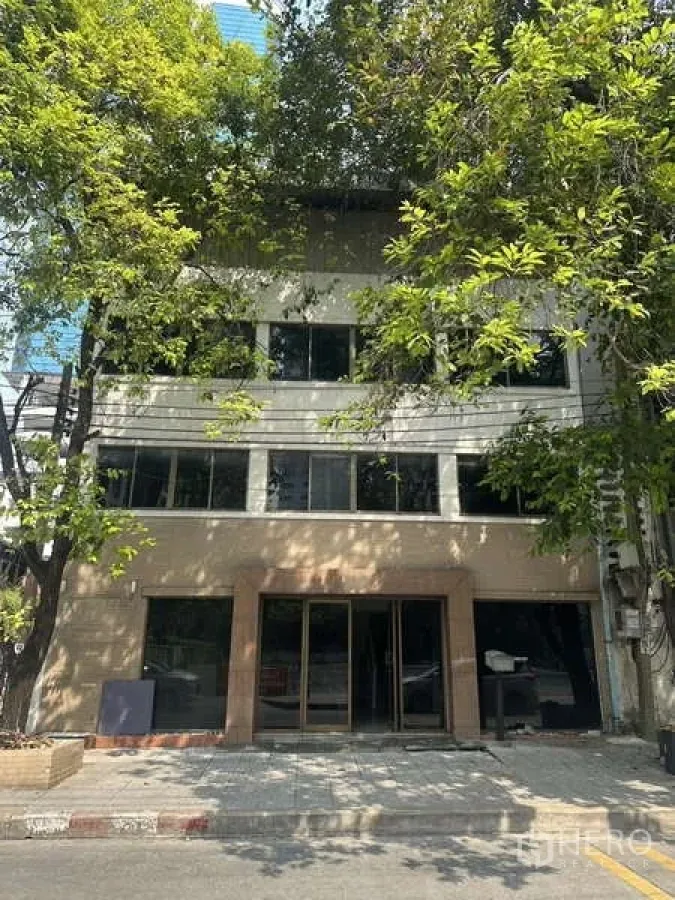Shophouse for rent in Khlong Toei, Bangkok - Street‑facing multi‑storey shophouse exterior with wide glass frontage shaded by trees in Ekkamai.