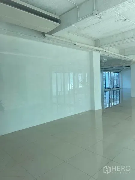 Office Space for rent in Khlong Toei, Bangkok - Empty white office interior with exposed ceiling, wall-mounted air-conditioning and reflective tile flooring.