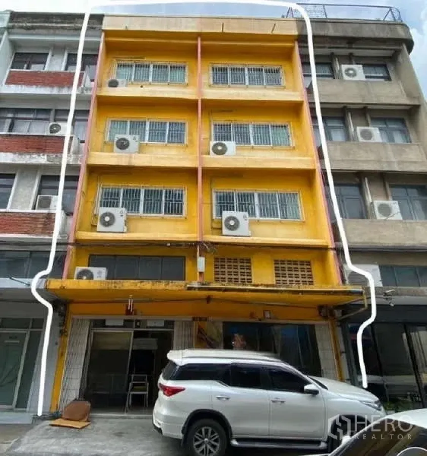 店屋 出租或出售在Watthana, Bangkok - 黄色多层店屋外立面，装有多台空调，门前可停车。