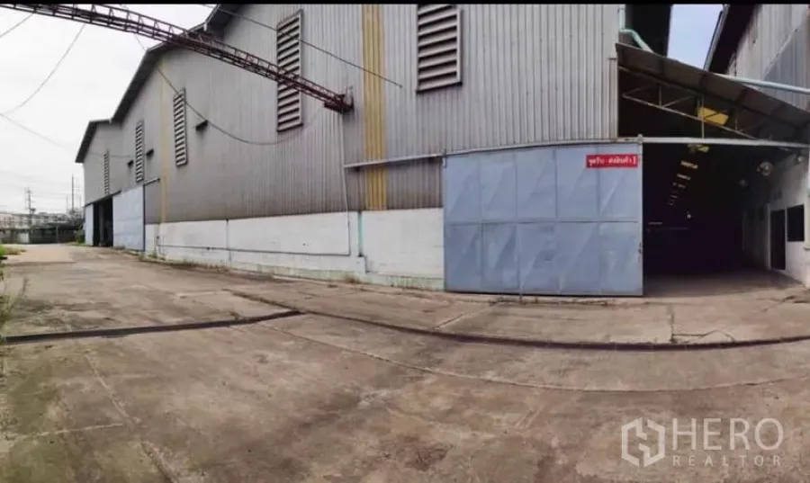 Factory for rent in Krathum Baen, Samut Sakhon - Large metal-clad factory exterior with wide sliding gate and a concrete yard.