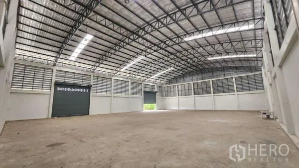 Factory for rent in Ban Phaeo, Samut Sakhon - Spacious factory interior with high arched steel roof, skylight strips, louvered vents and a large roller shutter door.
