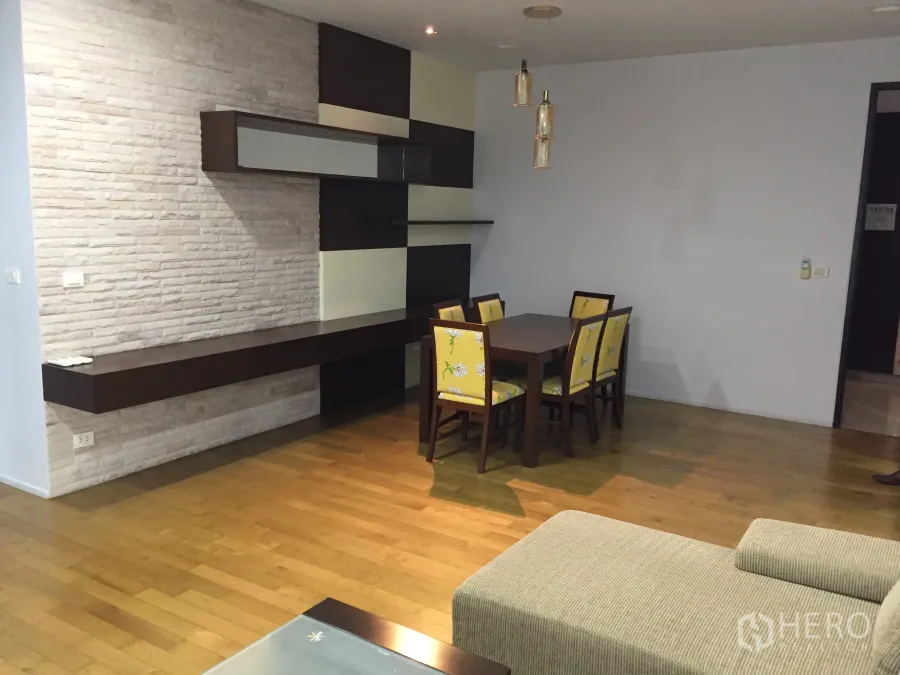 Condominium for rent in Watthana, Bangkok - Dining area with six-seat table, floating shelves and a brick feature wall on hardwood floors.