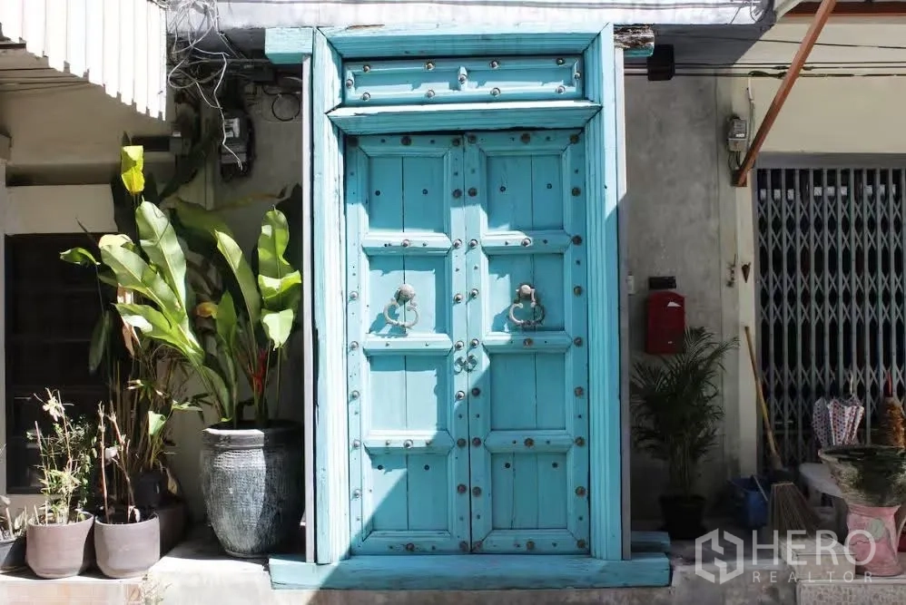 联排别墅 for rent in Watthana, Bangkok - 外立面青绿色双扇木门，入口旁摆放盆栽。