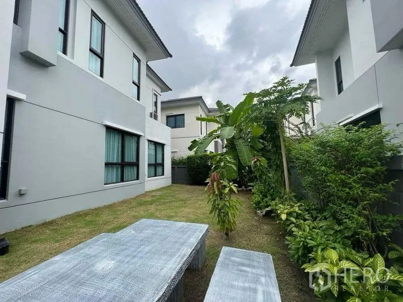 独立式住宅 出租在Mueang Nonthaburi, Nonthaburi - 后院草坪，绿篱与香蕉树环绕并设户外座椅。