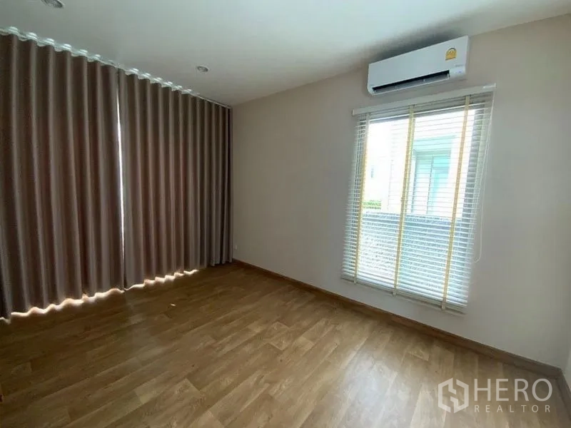 Townhouse for rent in Prawet, Bangkok - Bedroom with wood flooring, blinds, long drapes and wall-mounted air conditioner.