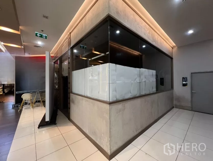 Retail Space for rent - Glass-walled corner retail unit with tiled corridor and warm ceiling lighting inside a mall.