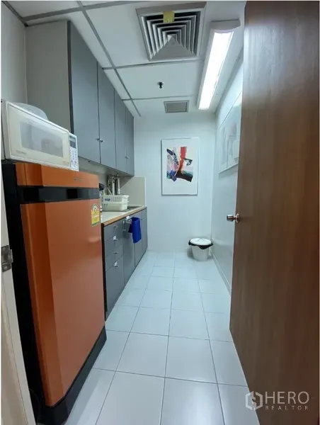 Office Space for rent in Khlong Toei, Bangkok - Office pantry with orange refrigerator, microwave, sink and grey upper cabinets on white tile flooring.