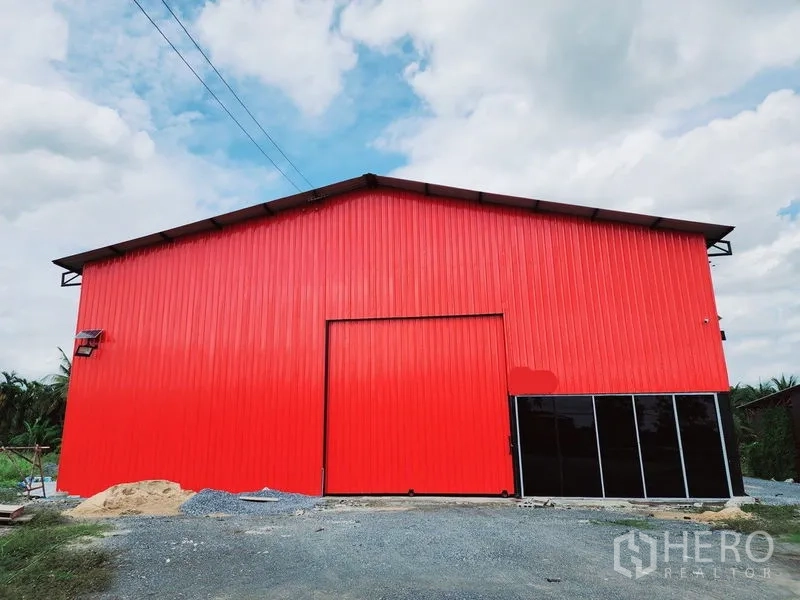 Warehouse for rent in Sam Phran, Nakhon Pathom - Front elevation of the red metal-clad warehouse with sliding door and black glass panels.