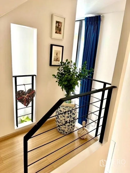 Townhouse for rent in Suan Luang, Bangkok - Stair landing with black handrail, wood flooring, and a decorative plant.