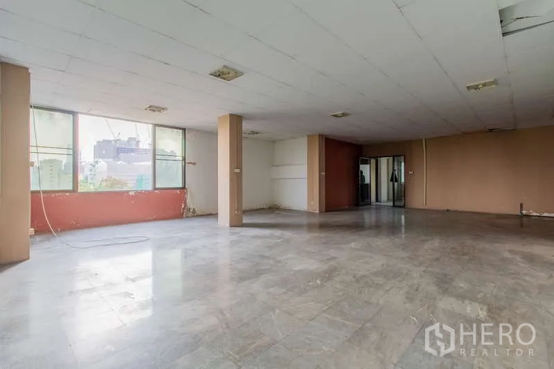 办公空间 出租或出售在Huai Khwang, Bangkok - 开放办公区，宽大窗户、结构柱与灰色地砖，可见城市景观。