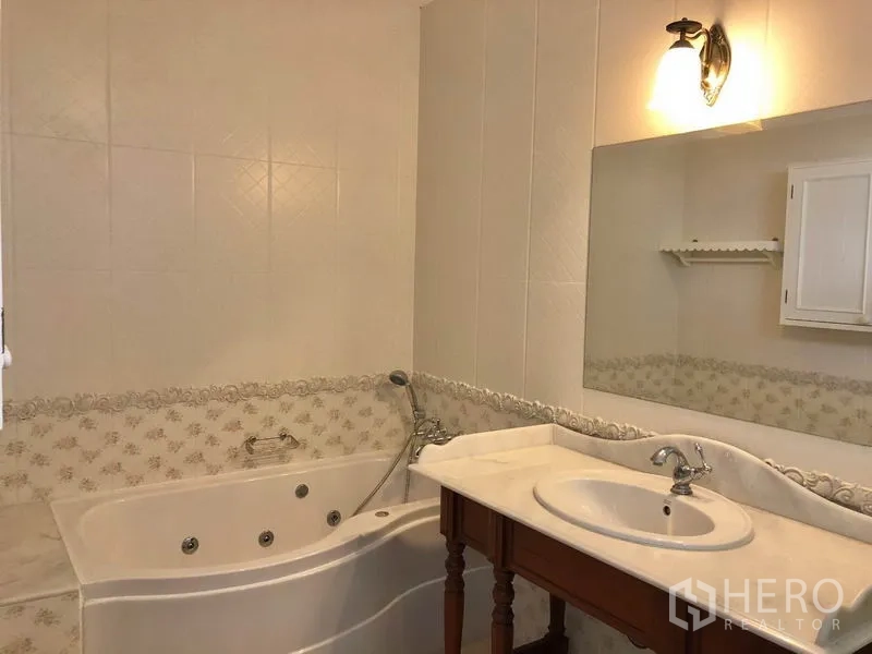 Detached House for rent in Mueang Samut Prakan, Samut Prakan - Bathroom with whirlpool bathtub, large mirror, marble‑top vanity and wall sconce lighting.