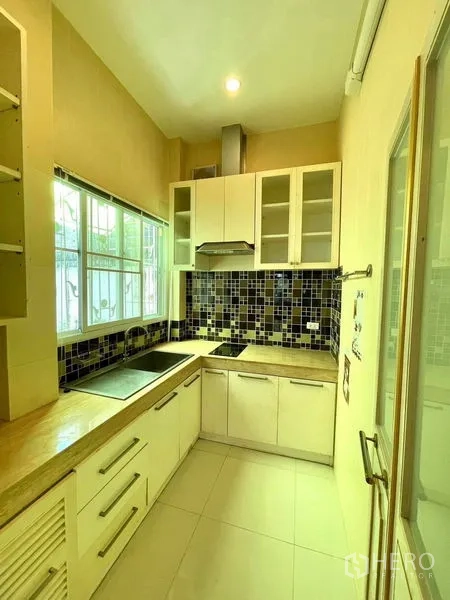 Townhouse for rent in Saphan Sung, Bangkok - Compact U‑shaped kitchen with mosaic backsplash, white cabinetry, range hood and a window for natural light.