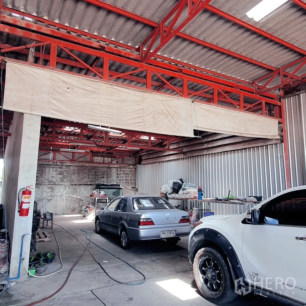 Warehouse for rent in Lam Luk Ka, Pathum Thani - Covered workshop bay inside the warehouse with parked cars and red steel trusses.