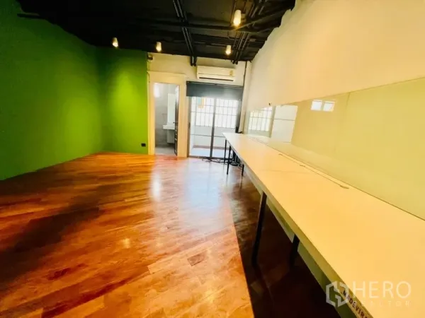 Office Space for rent in Khlong Toei, Bangkok - Workroom with long built-in desks, a green accent wall and a doorway to the bathroom.